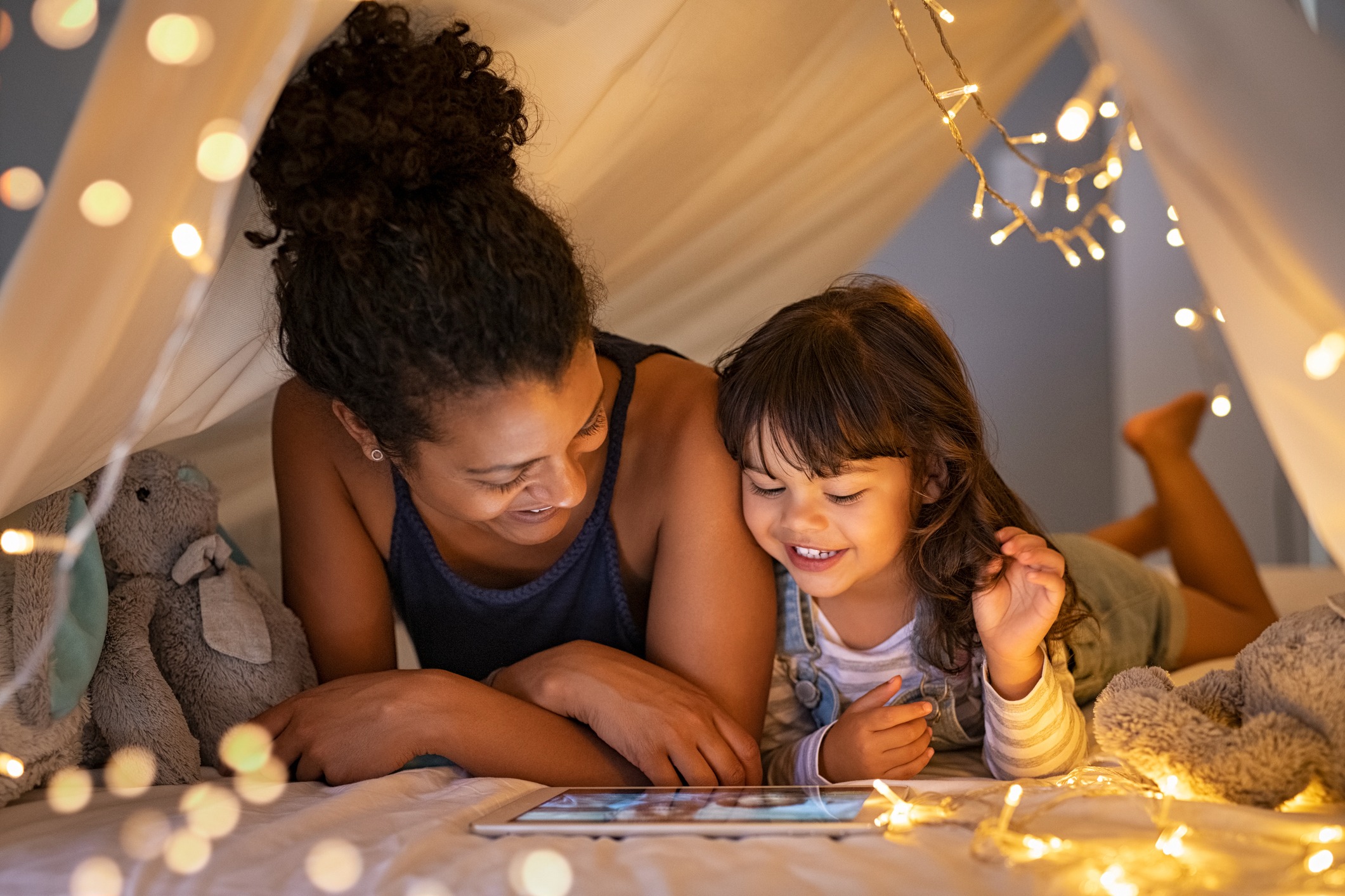 A woman and child reading together under a blanket fort