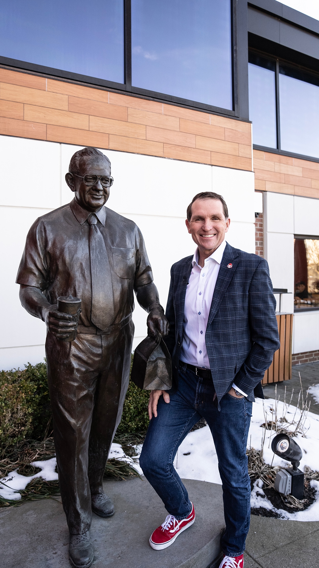 Kirk Tanner in red sneakers standing beside a bronze statue of Wendy’s founder Dave Thomas