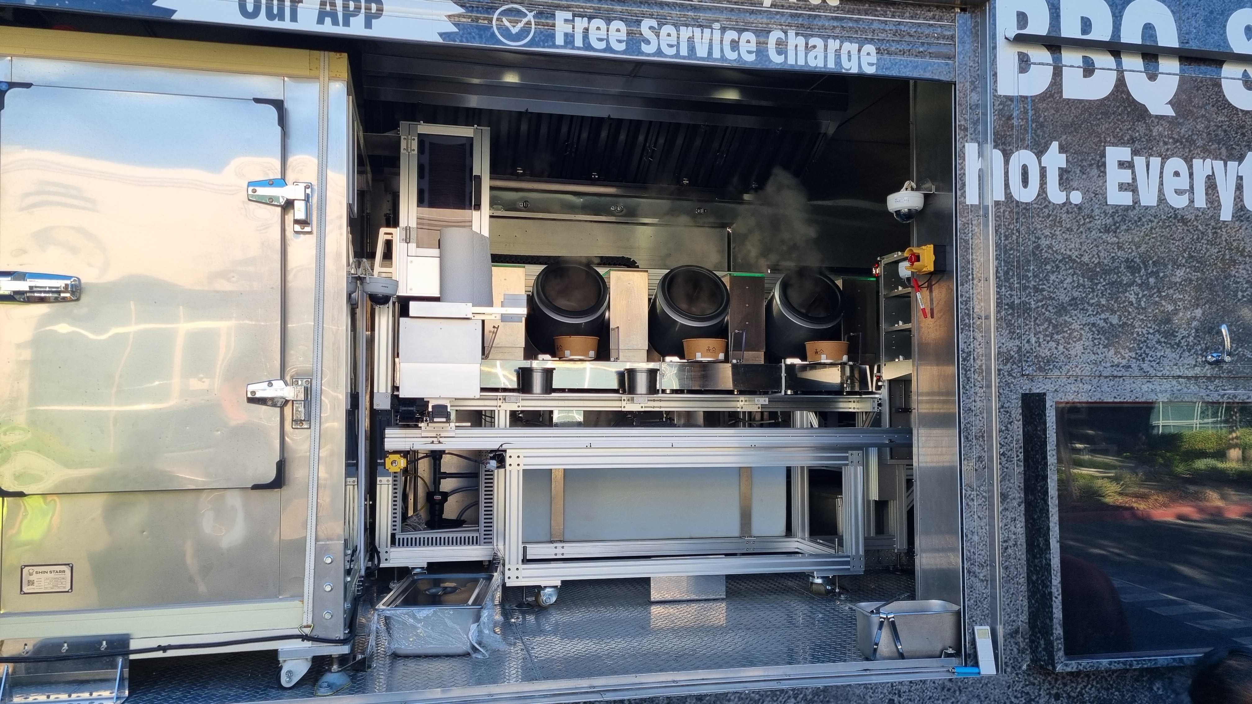 The open side of an OLHSO robotic food truck showing a row of automated cooking vessels