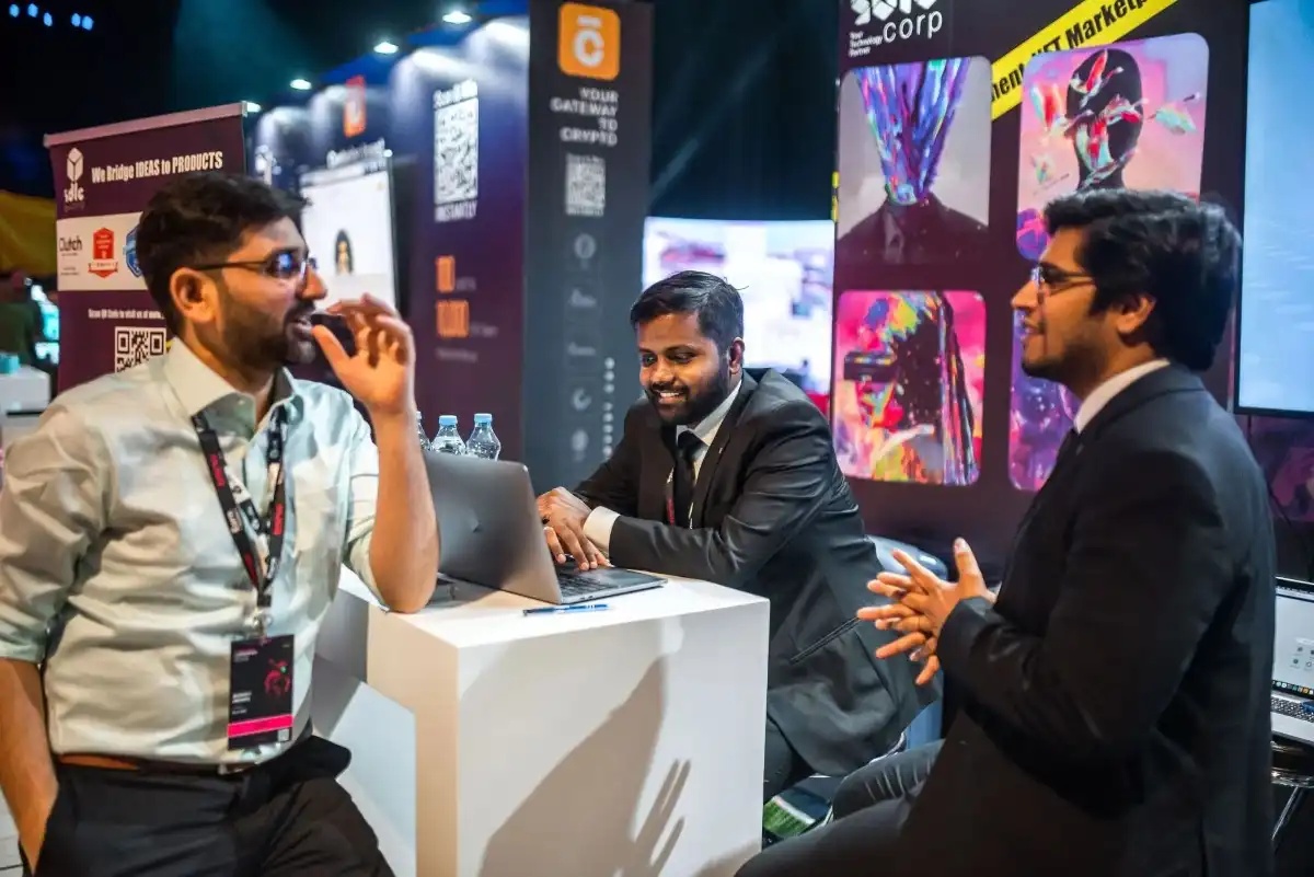 Kishan Srivastava seated at the centre of a conversation at an SDLC Corp exhibition booth