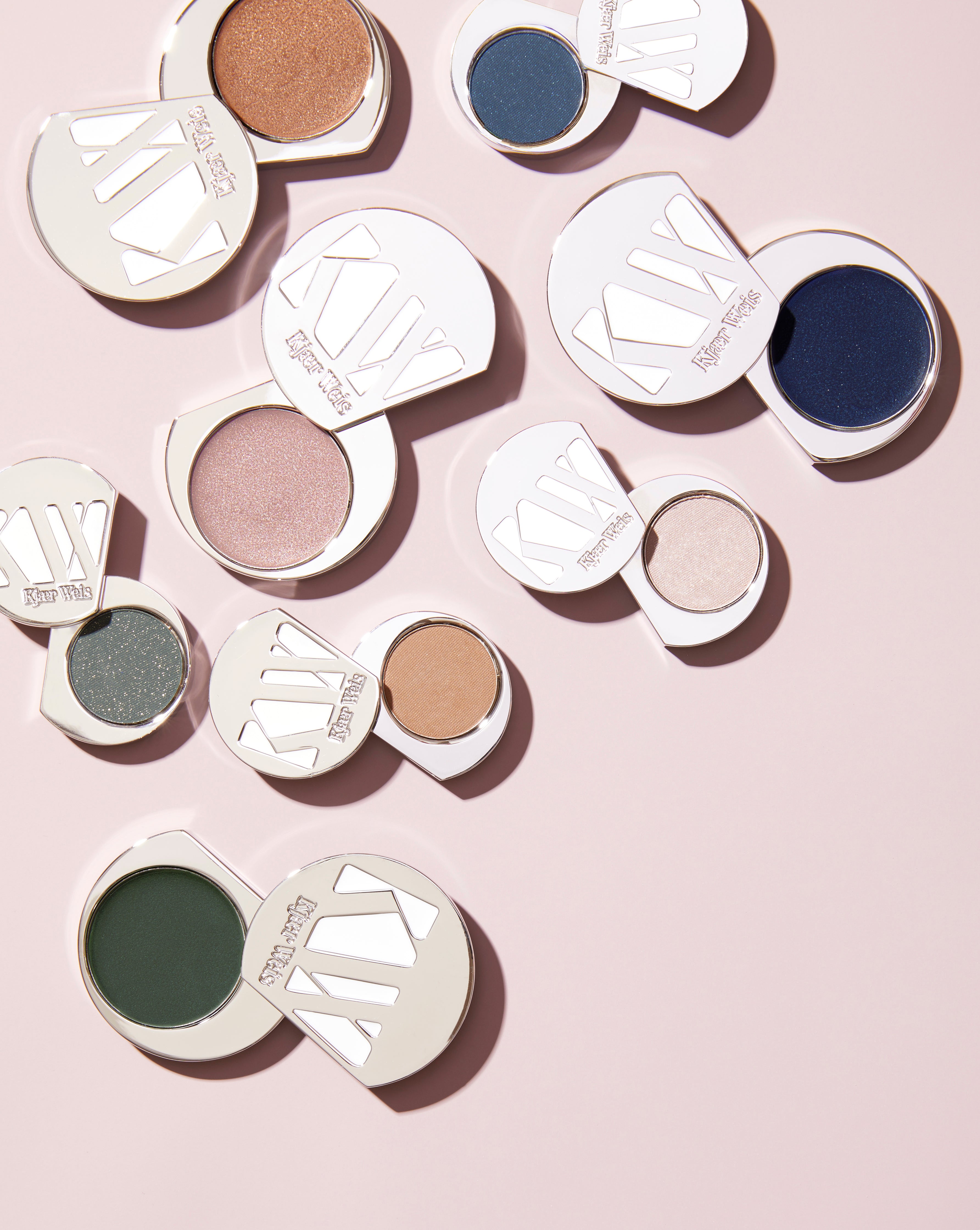 Open silver eye shadow compacts with blue, gold and neutral colors on pink