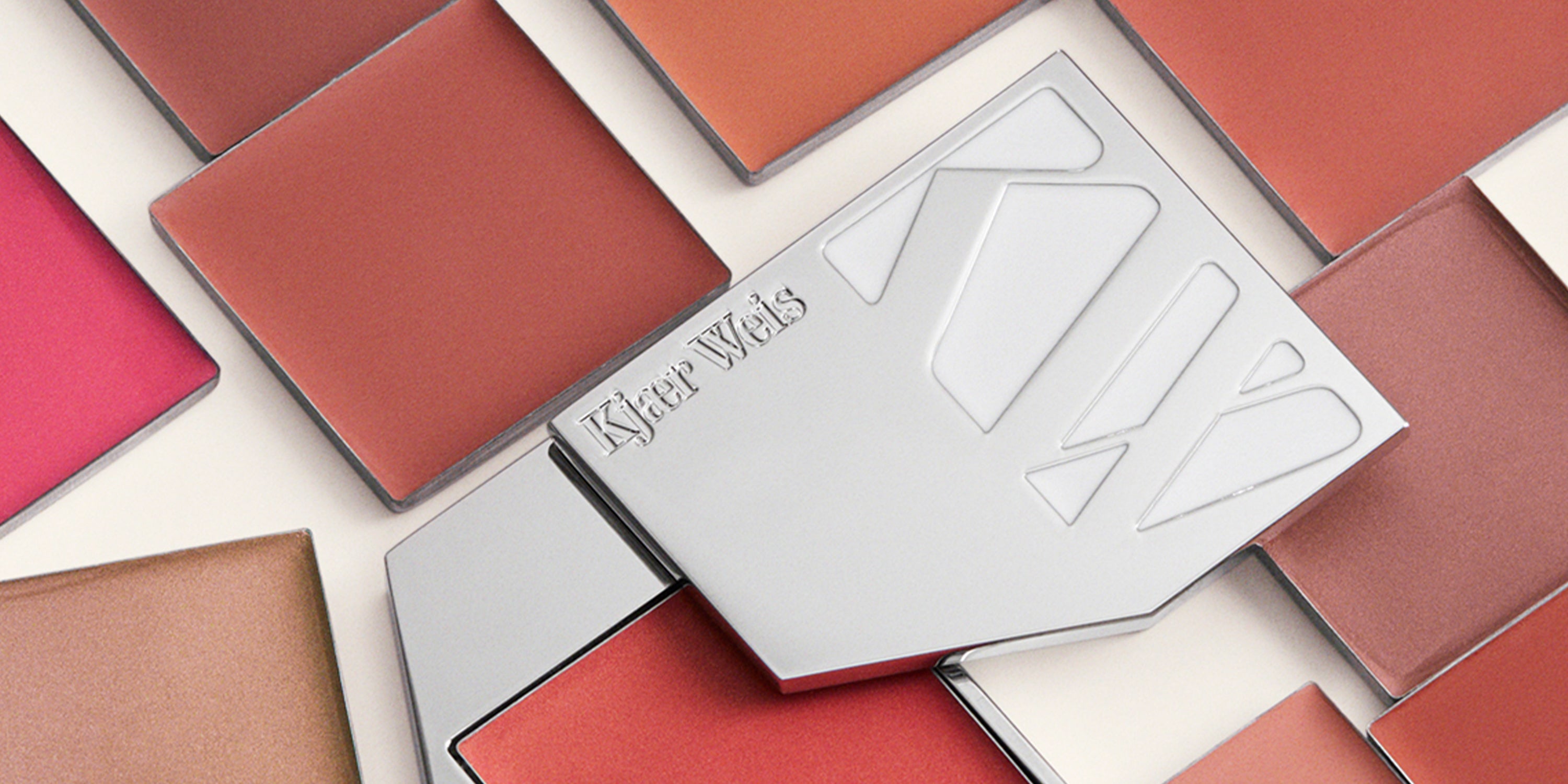 Warm pink and coral cream blush pans arranged around a silver Kjaer Weis compact