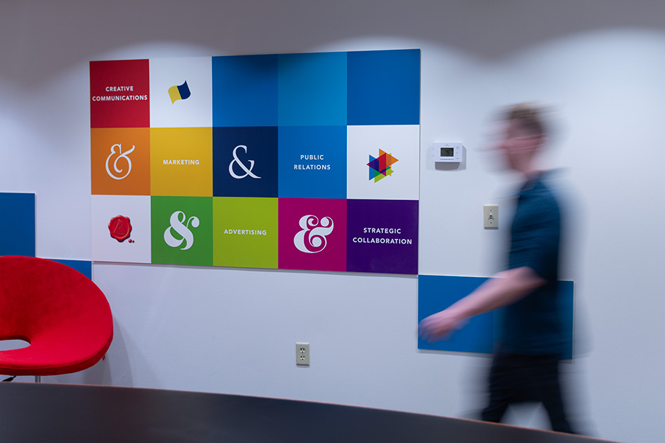 A colorful wall of marketing and communications symbols inside the Kleidon office, with a team member walking past