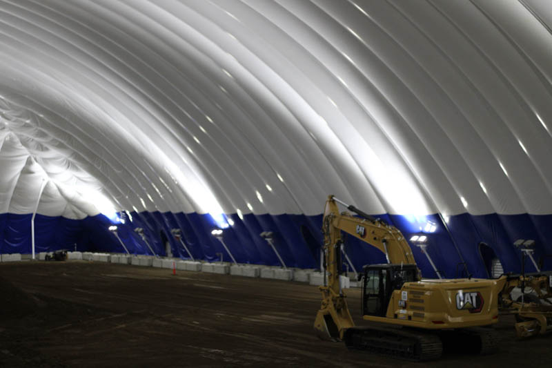 A yellow excavator on the dirt floor beneath Knife River’s inflated training dome