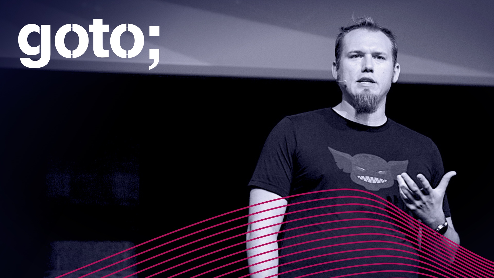 Kolton Andrus speaking onstage in a Gremlin T-shirt in GOTO conference artwork