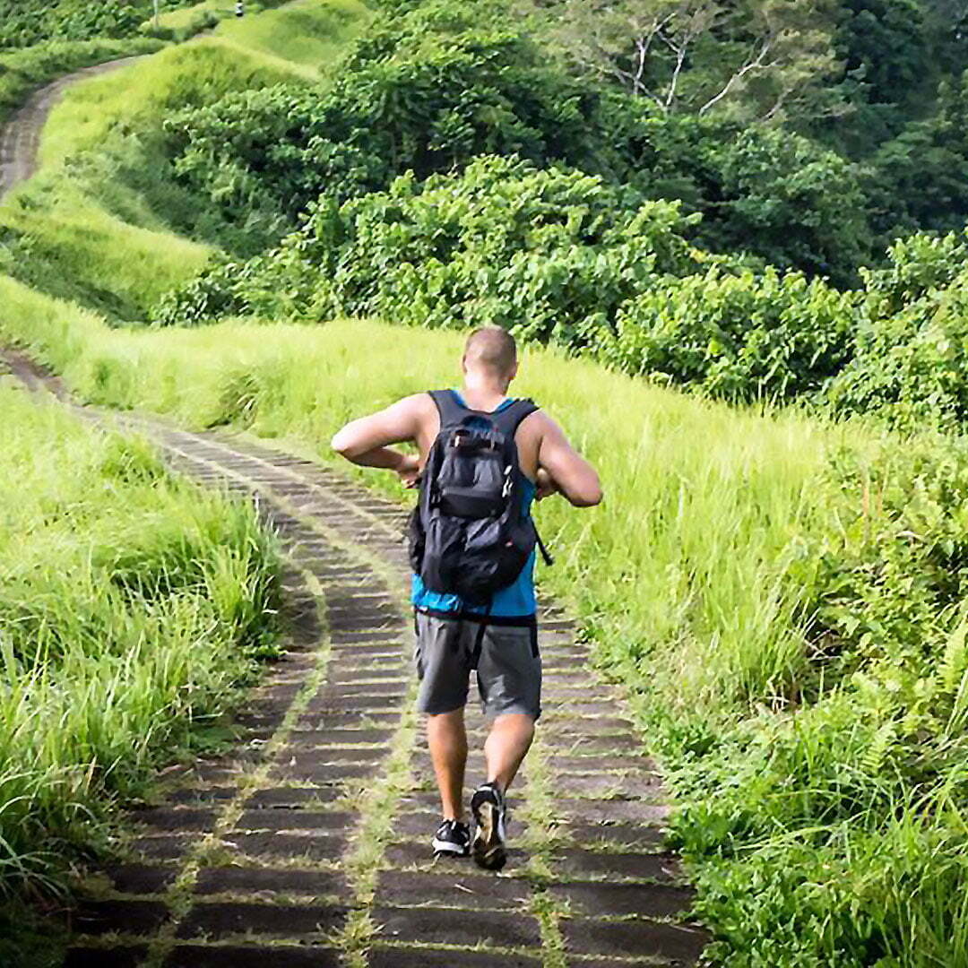 Konrad Waliszewski walking down a green hillside path with a backpack