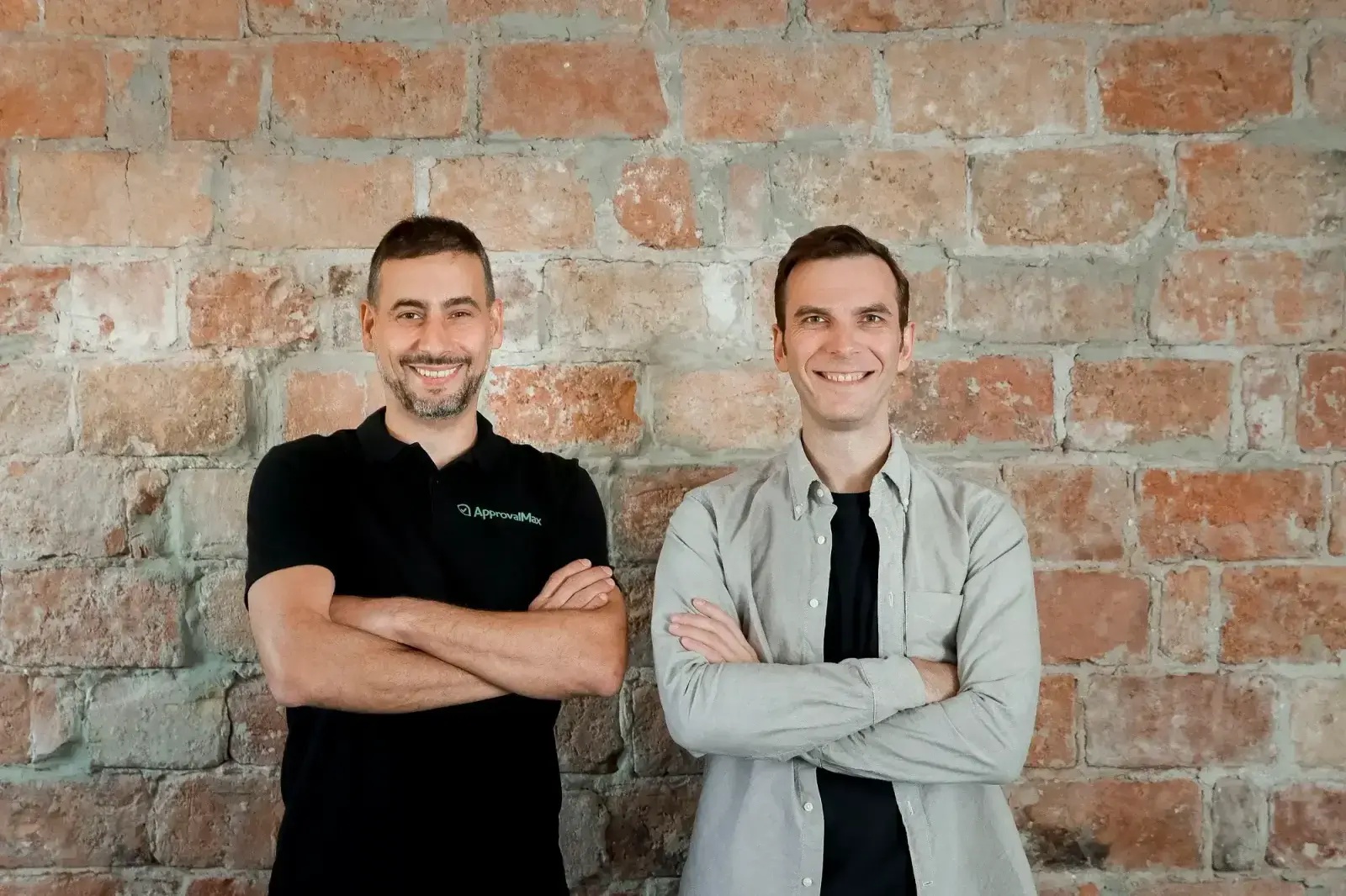 ApprovalMax co-founders Peter Volynsky, left, and Konstantin Bredyuk, right, standing against a brick wall