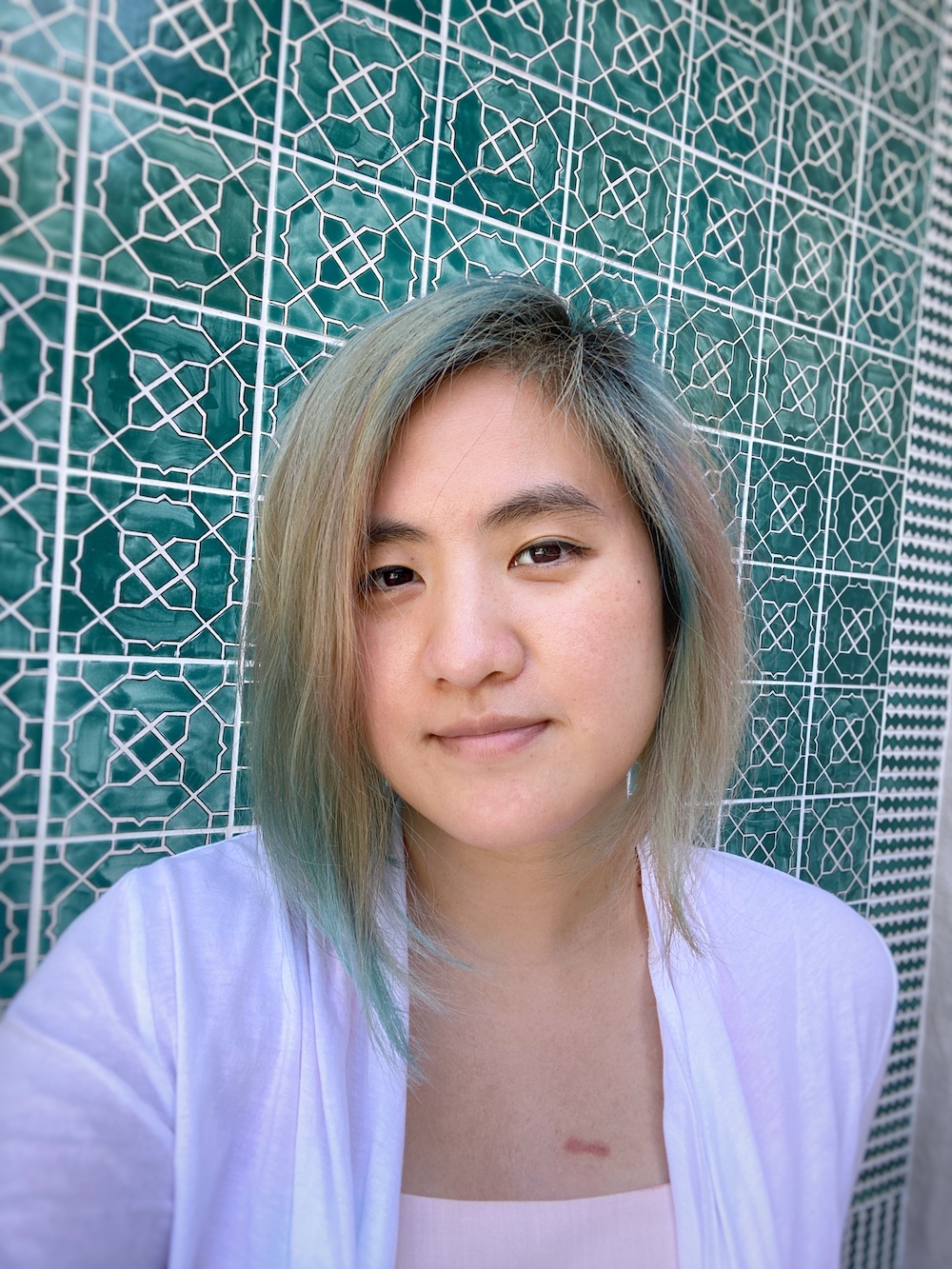 Konsult co-founder Jing Jin in front of a patterned teal tile wall