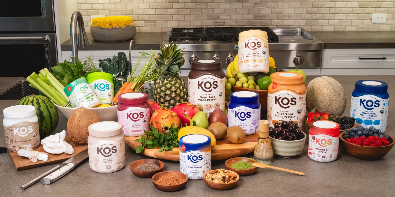 Colorful KOS nutrition tubs arranged with fruit, vegetables and pantry ingredients in a kitchen