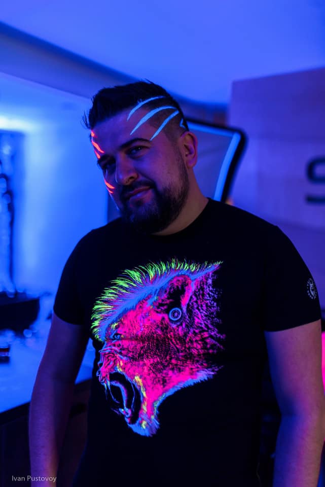 Makarov in blue lighting wearing a brightly colored parrot T-shirt