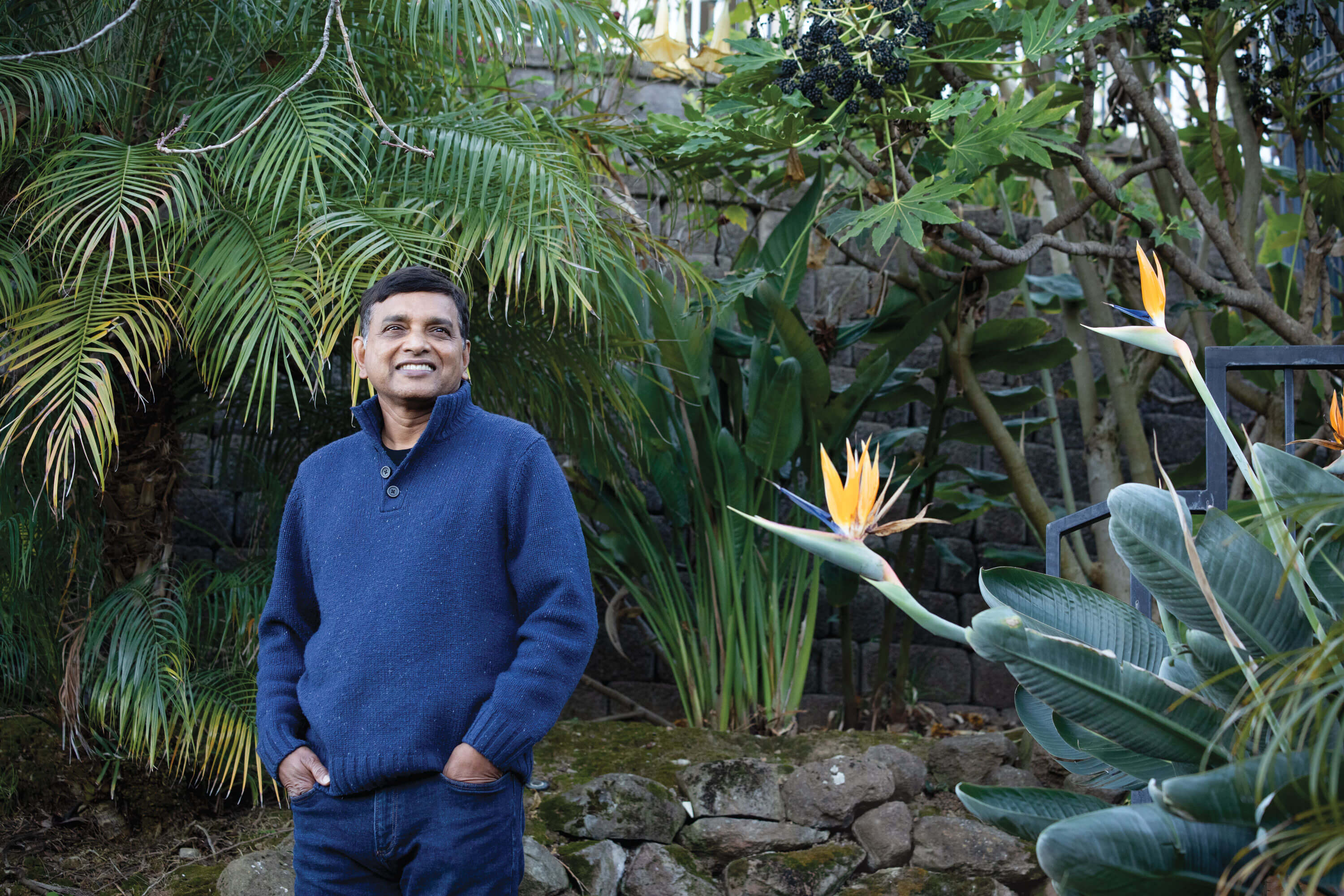 Krish Ramakrishnan in a blue sweater standing among garden plants