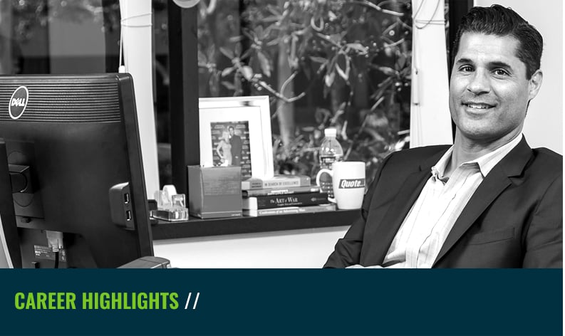 Krish Coughran seated beside a computer in an office, in a black-and-white company photograph