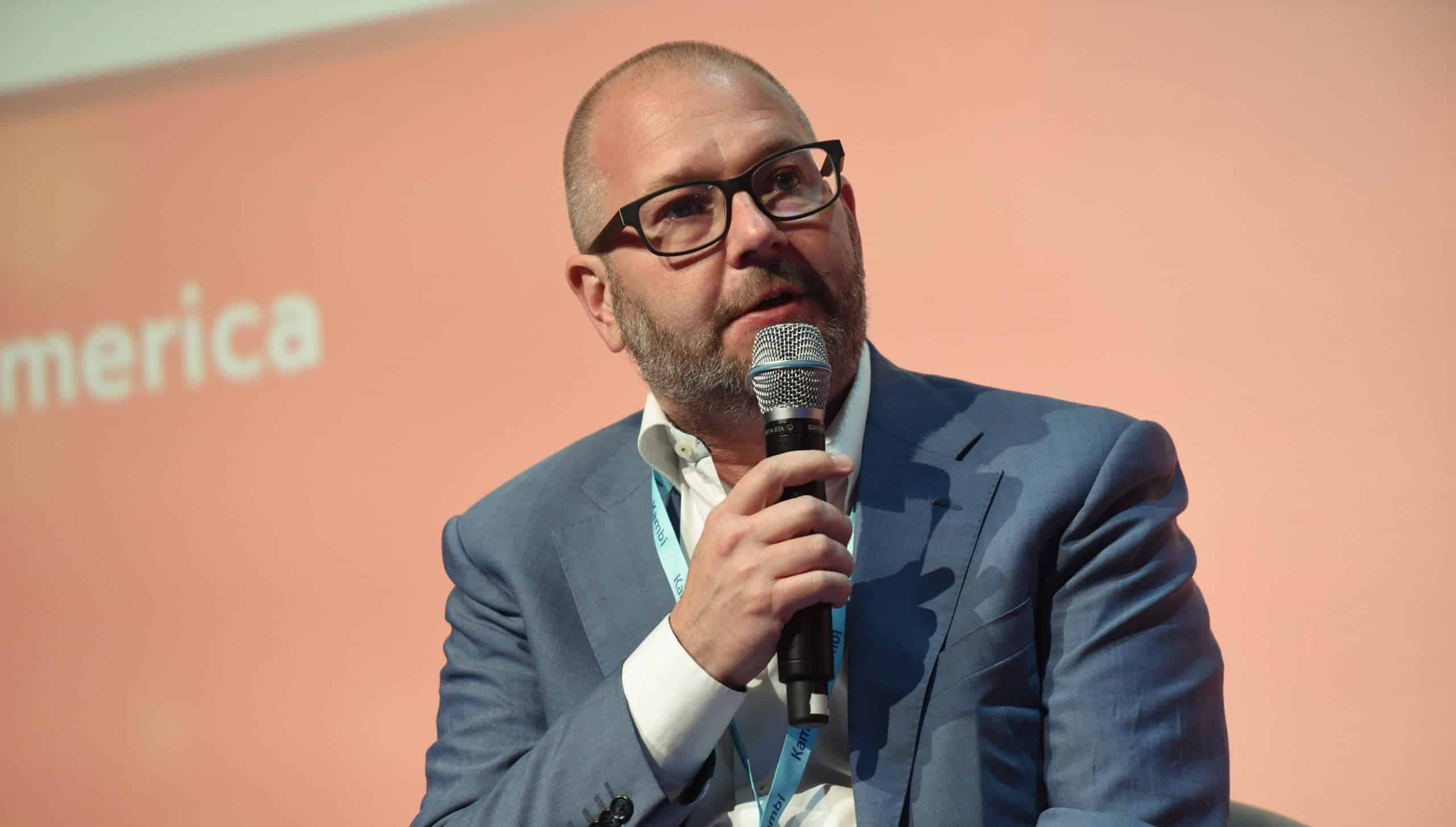 Kristian Nylén speaking into a microphone at a US conference, against a peach-coloured backdrop.
