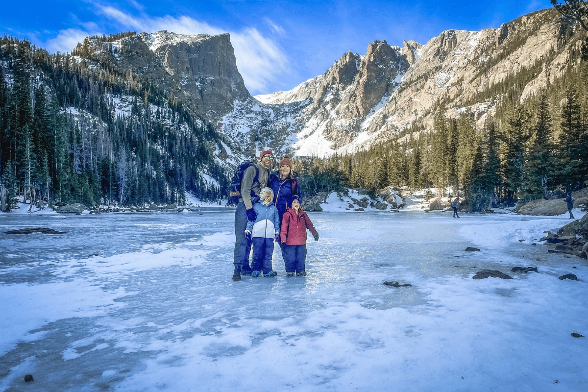 Kristin Tillack and her family standing on a frozen mountain lake beneath snowy cliffs