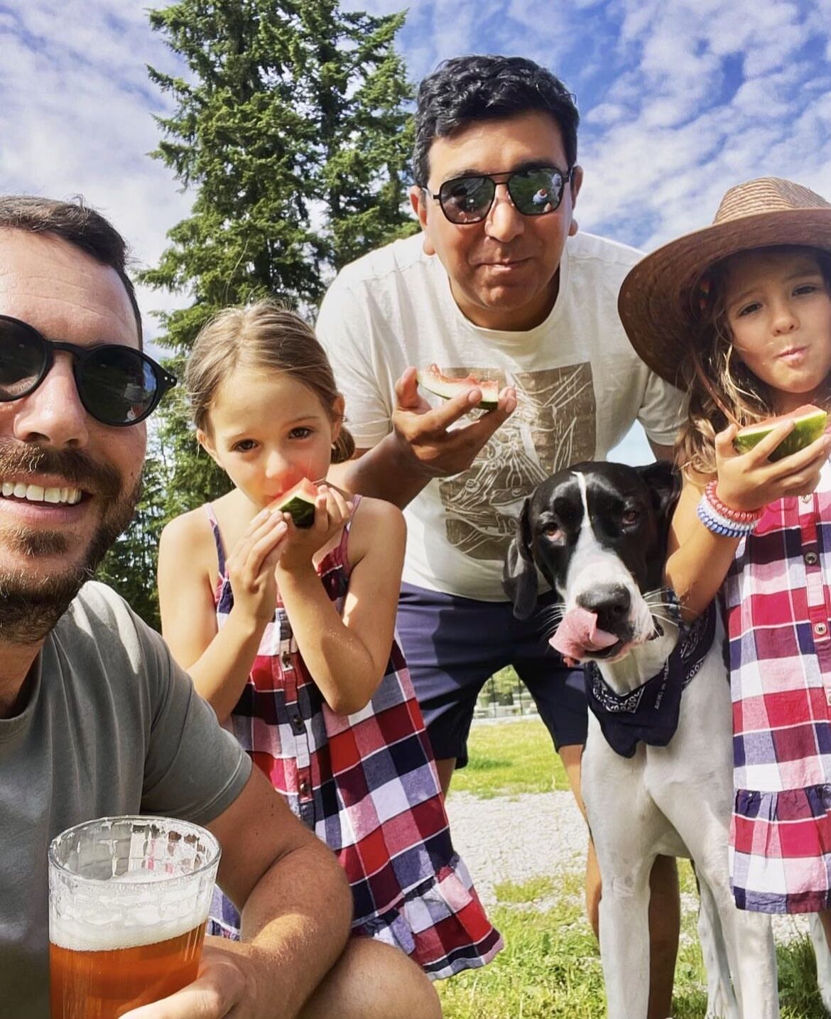 Kyle Arteaga outdoors with his husband, two daughters, and their dog, sharing watermelon