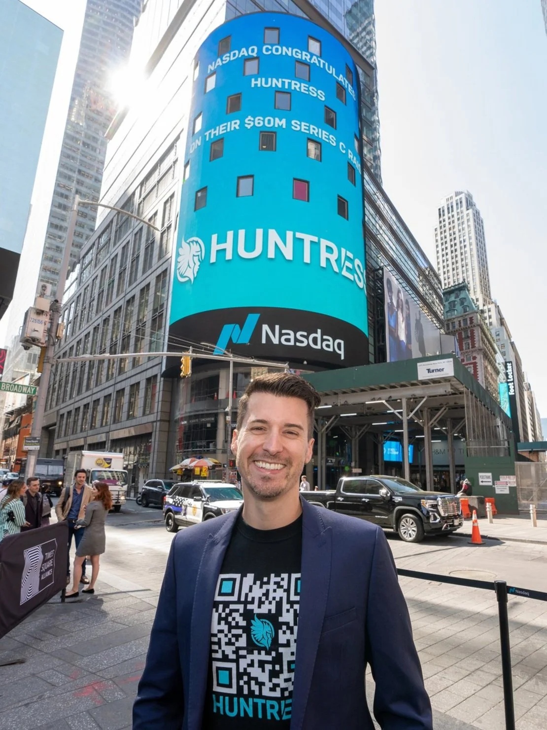 Kyle Hanslovan in Times Square beneath a Nasdaq screen congratulating Huntress on its $60 million Series C
