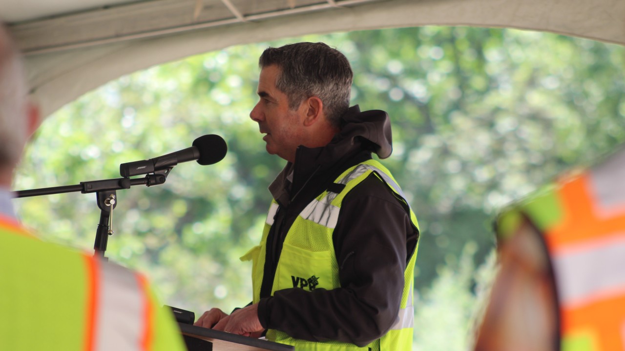 Kyle Larkin in a reflective vest speaking into a microphone at a construction event