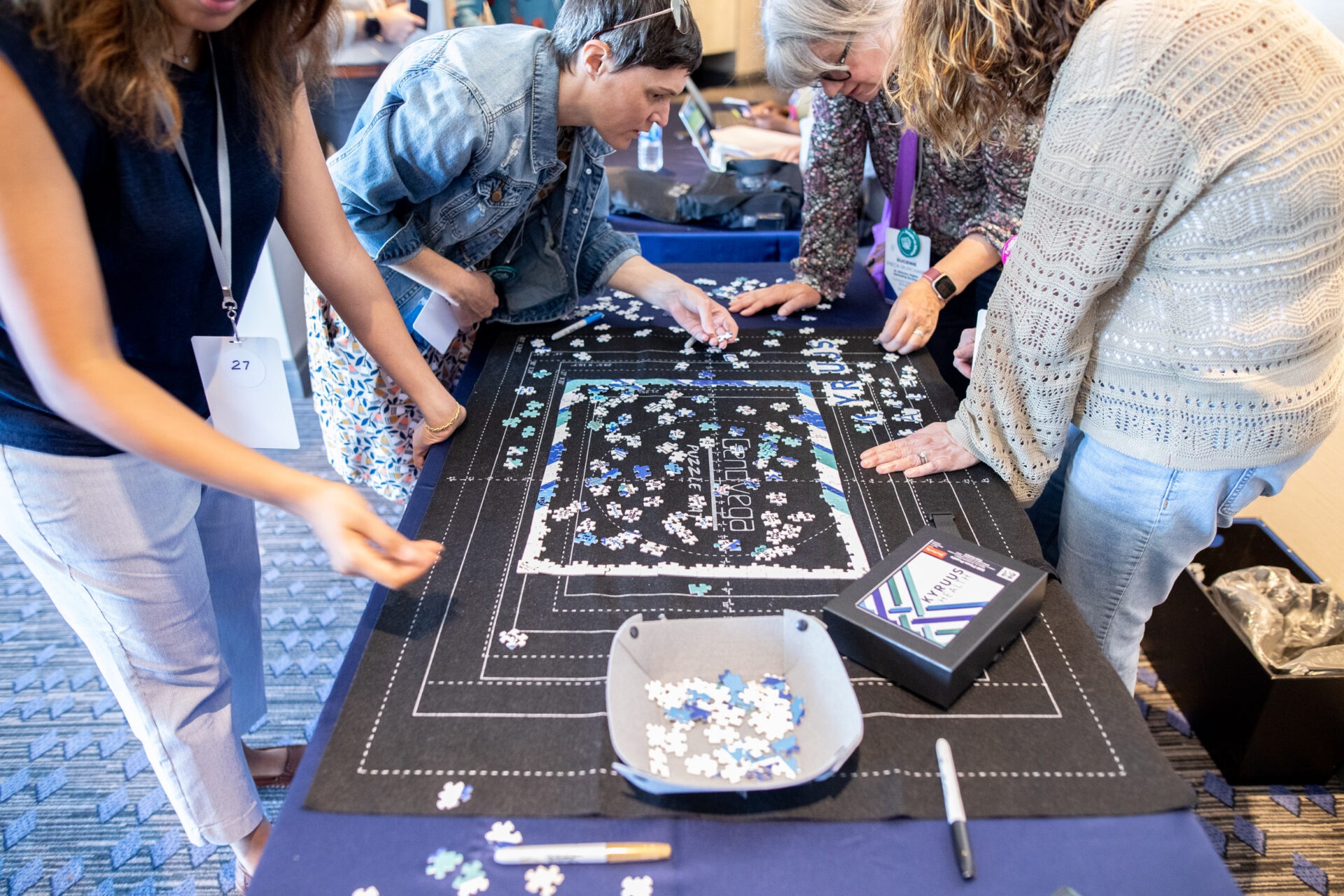 Participants in a Kyruus company event lean over a table to assemble a branded jigsaw puzzle