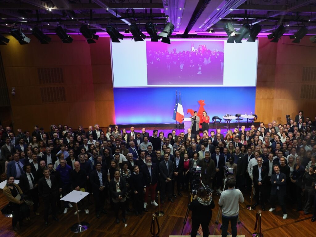 A large group of attendees at a French Tech gathering, with the rooster emblem on stage