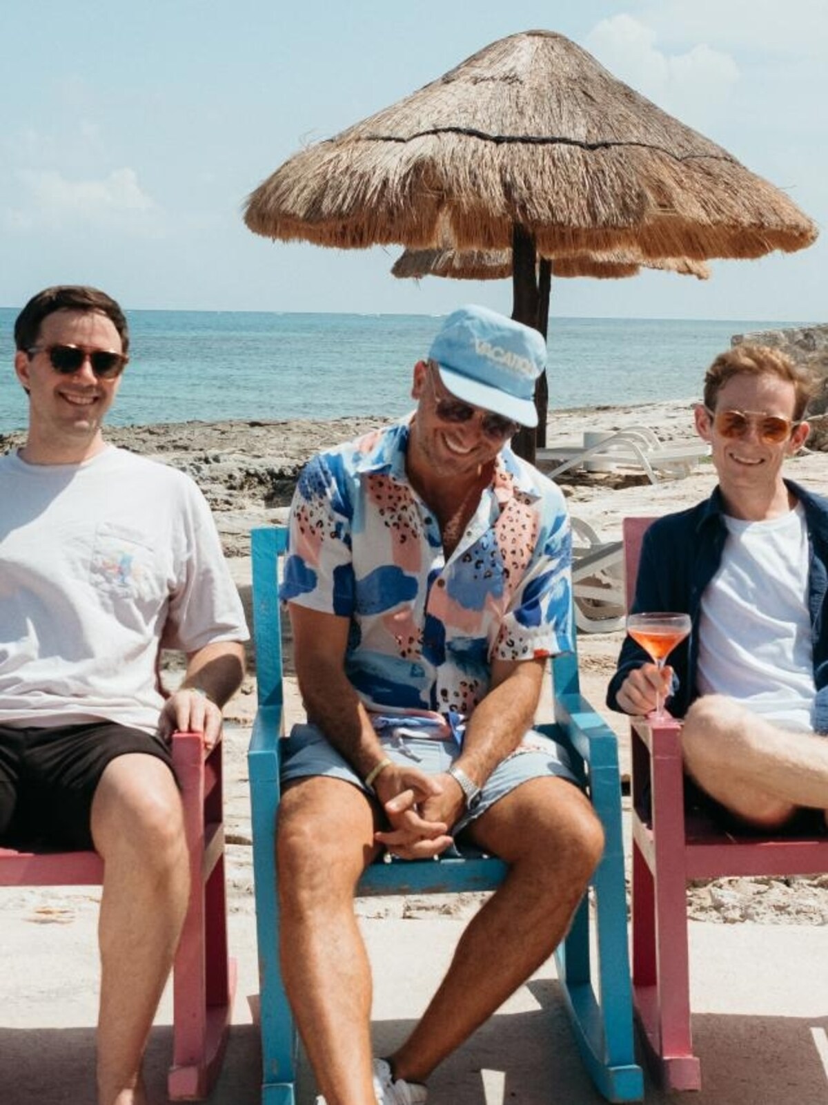 Vacation co-founders Dakota Green, Lach Hall and Marty Bell seated in colorful chairs on a beach