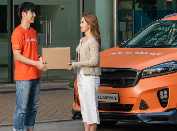 Lalamove promotional photograph of a driver handing a parcel to a customer beside an orange vehicle