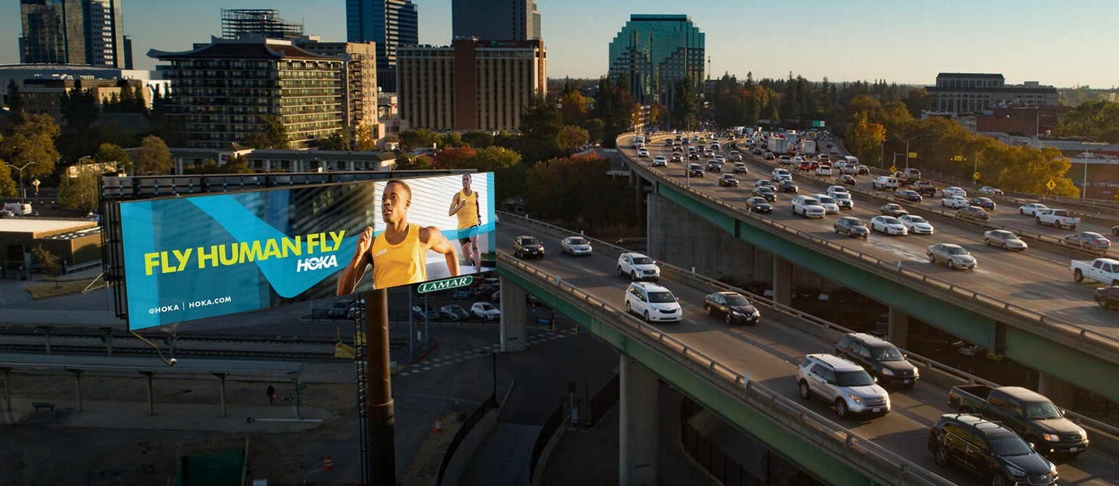 Hoka Fly Human Fly campaign displayed on a Lamar digital roadside billboard