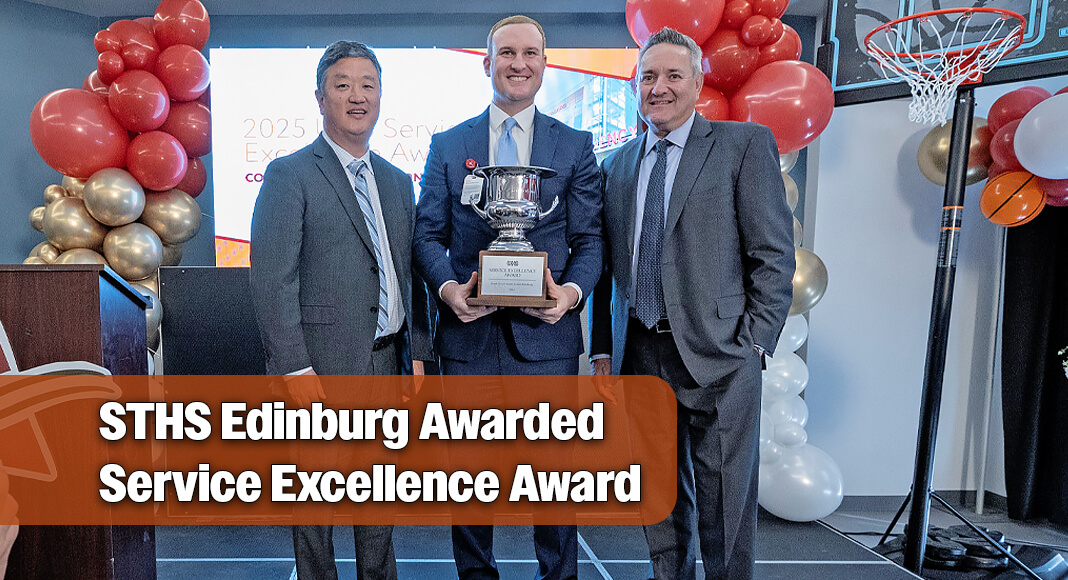 Lance Ames, center, holding an award beside UHS executives Edward Sim and Marc Miller, with balloons and a basketball hoop behind them