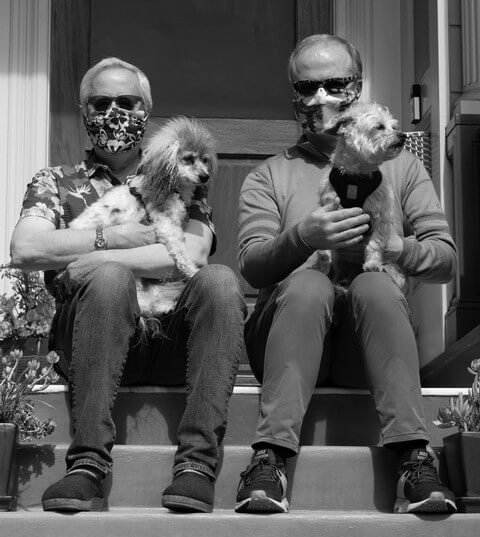 David Landis and Sean Dowdall seated on front steps, each holding dogs and wearing face masks