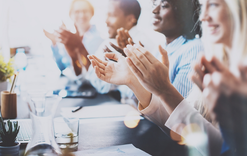A diverse business team applauding around a conference table