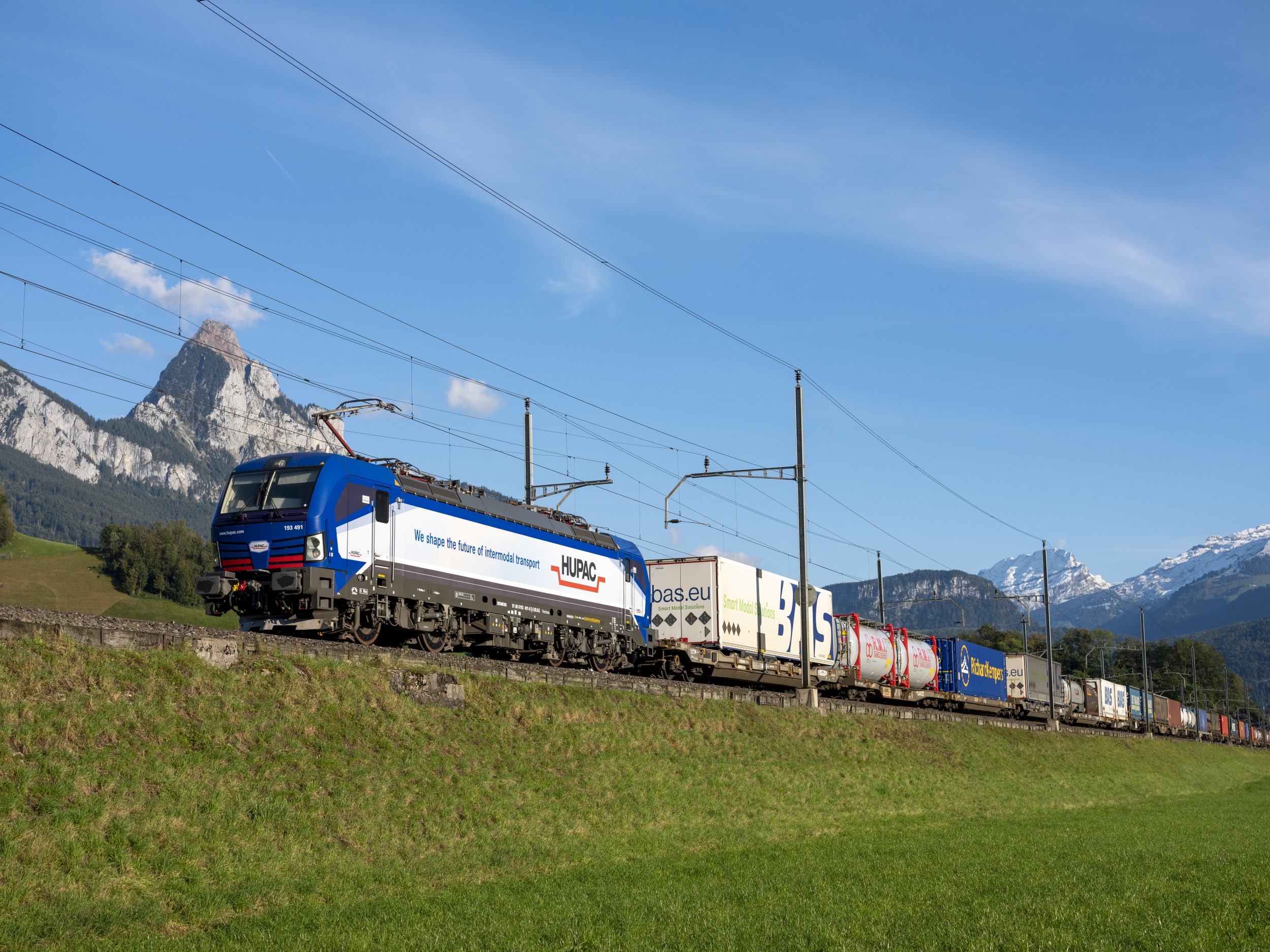 A Hupac intermodal freight train hauling containers through a mountain landscape
