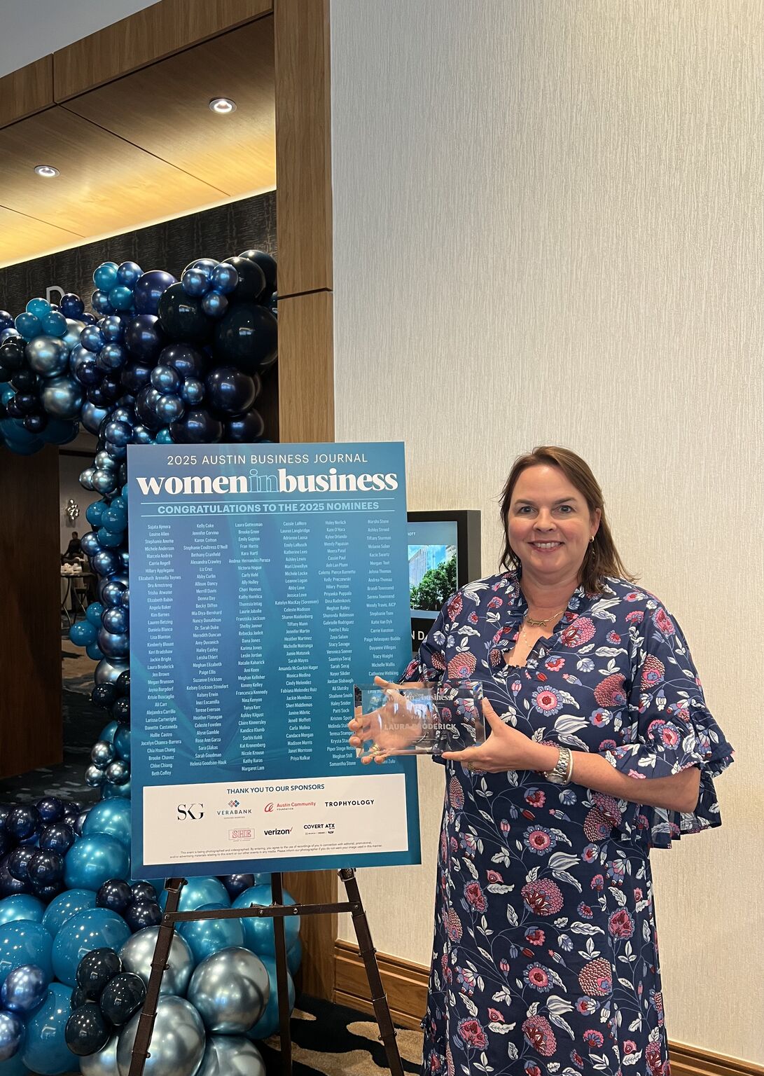 Laura Broderick holding her 2025 Austin Business Journal Women in Business award beside the event nominees board