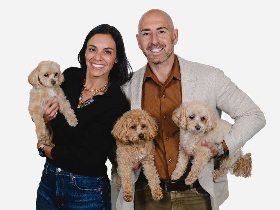 Lauren Izaks and Jamie Izaks smiling while holding three small office dogs