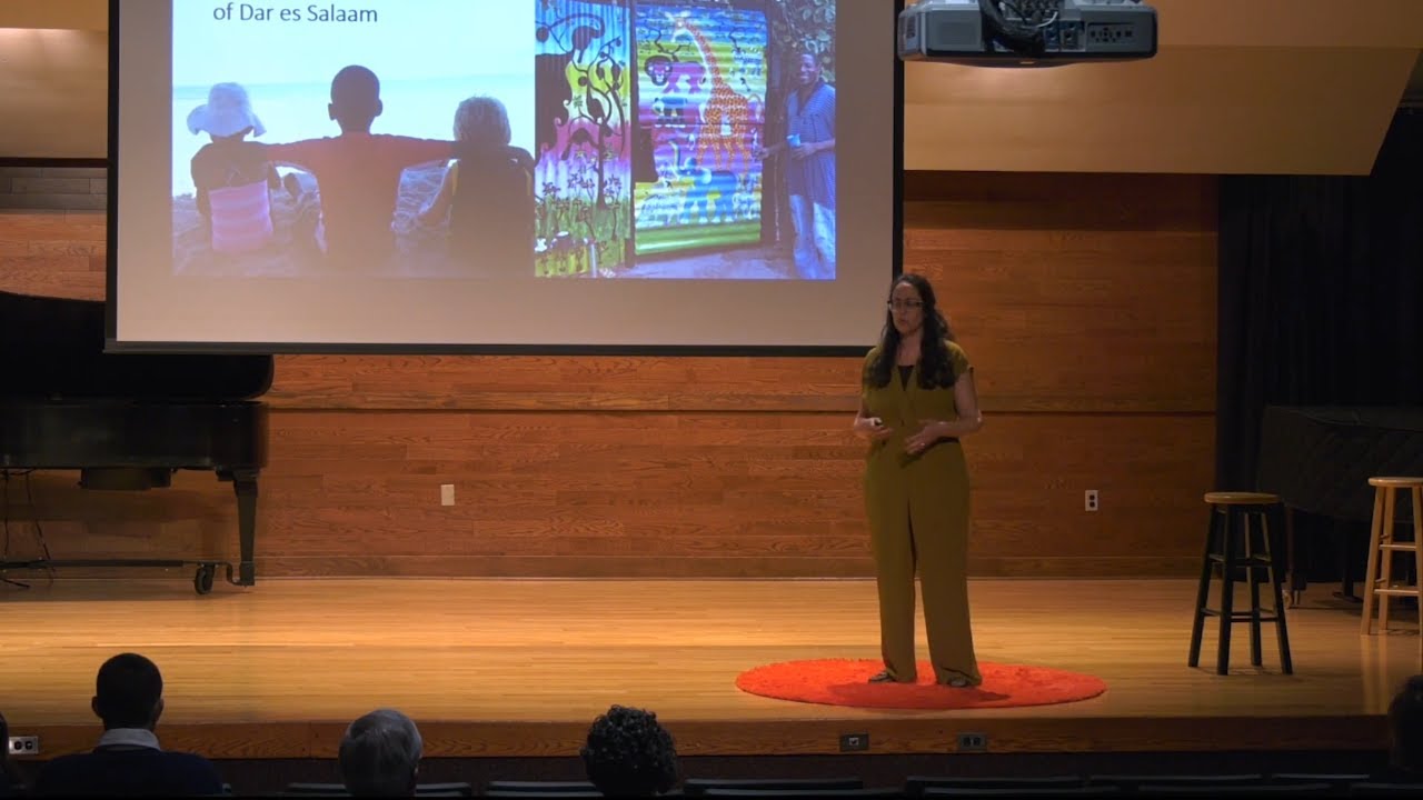 Lauren Schmidt speaking on a red TEDx stage with images from Dar es Salaam projected behind her