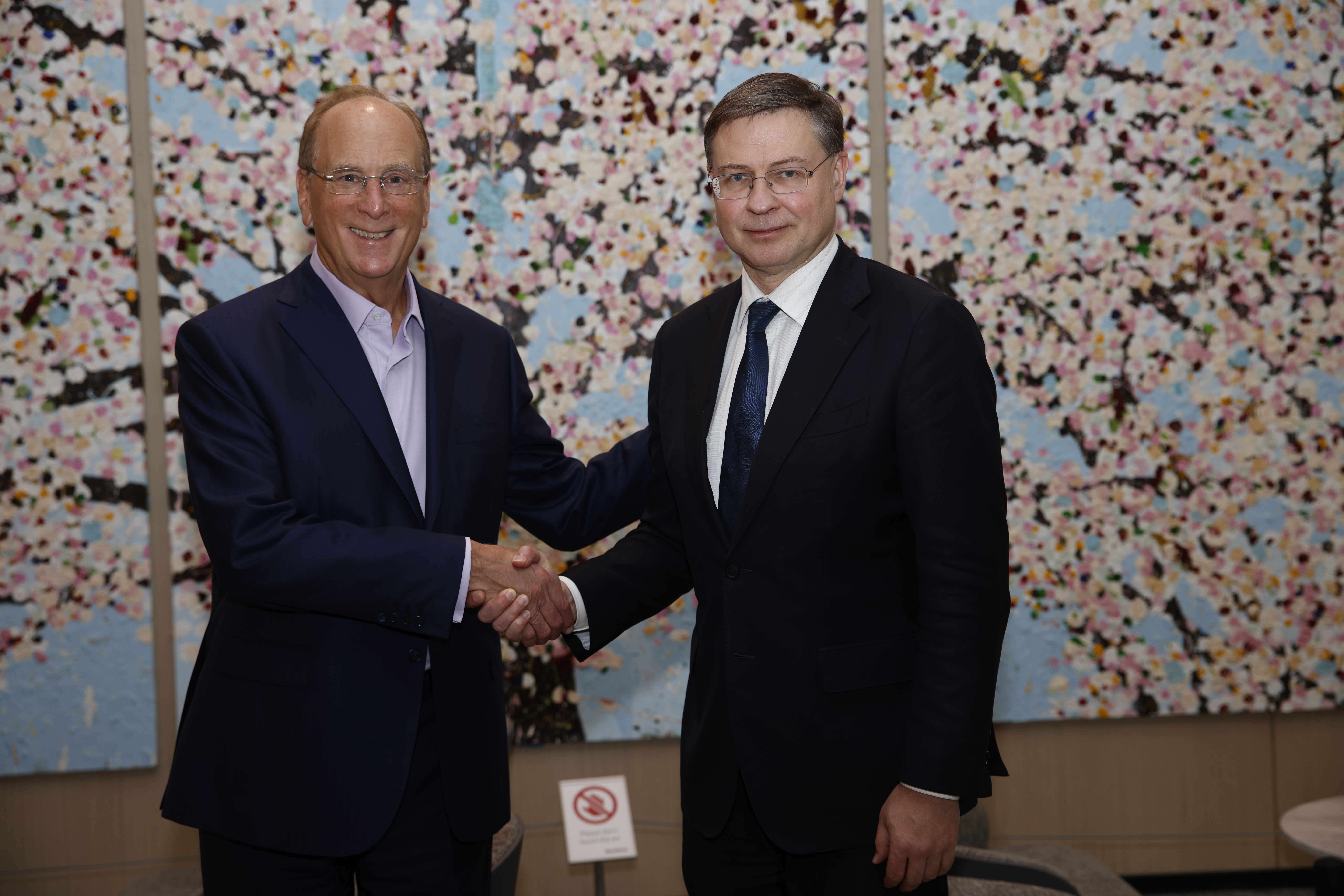 Larry Fink, left, shaking hands with European Commissioner Valdis Dombrovskis in front of a colorful painting in New York.