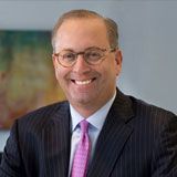 An archival portrait of Larry Sorrel wearing glasses and a pinstripe suit