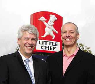 Lawrence Wosskow, left, and Simon Heath smiling beside a Little Chef sign
