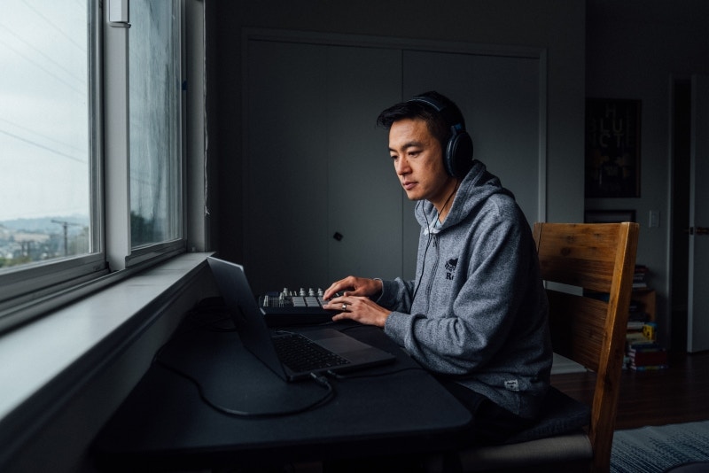 Lawrence Yeo wearing headphones and working on a laptop beside a window