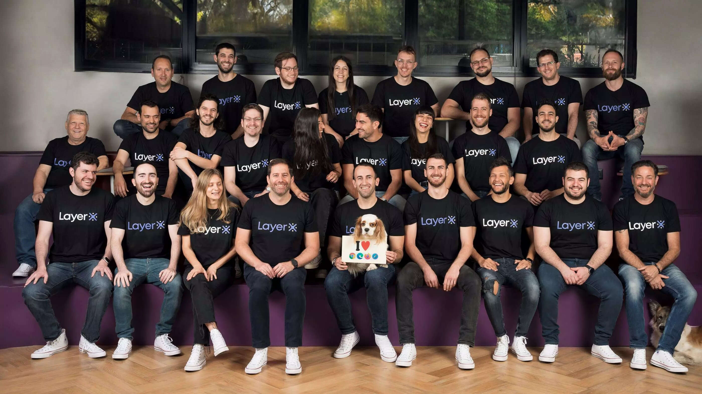 LayerX team in an office wearing company shirts, with a dog holding a browser sign