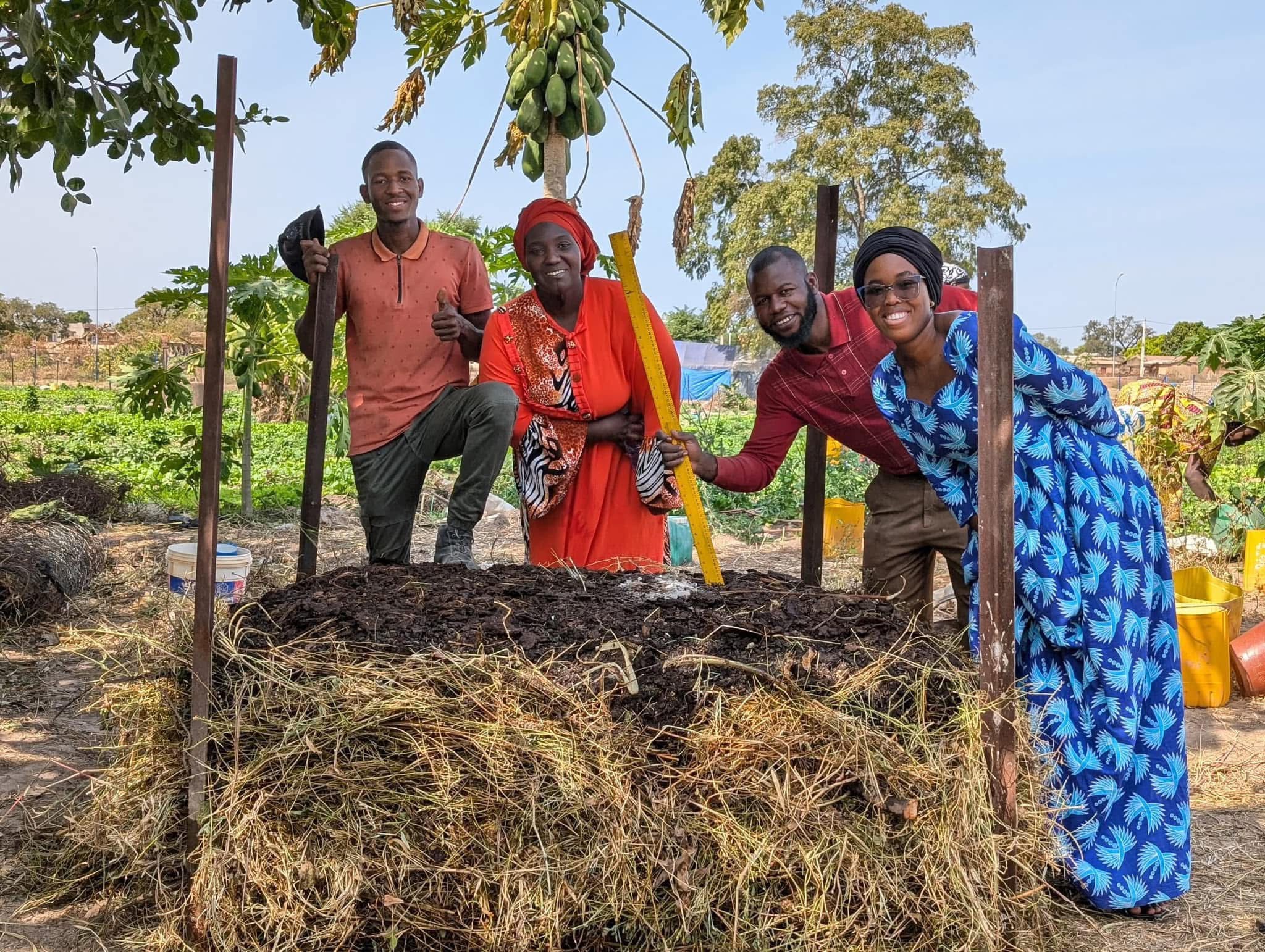 Four people beside a layered mound of organic material in a cultivated garden