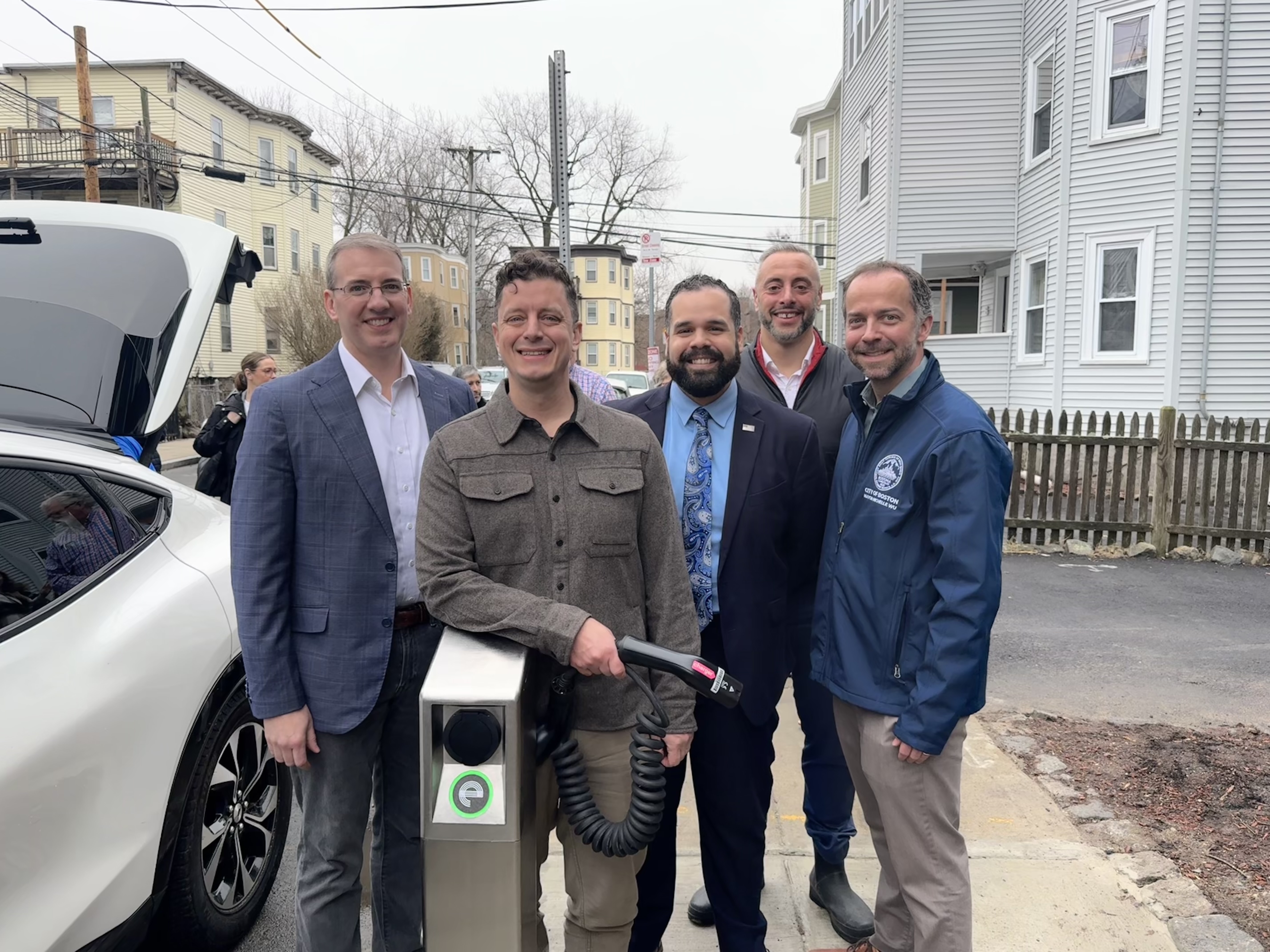 Participants gather beside an itselectric curbside charger and electric vehicle in Boston