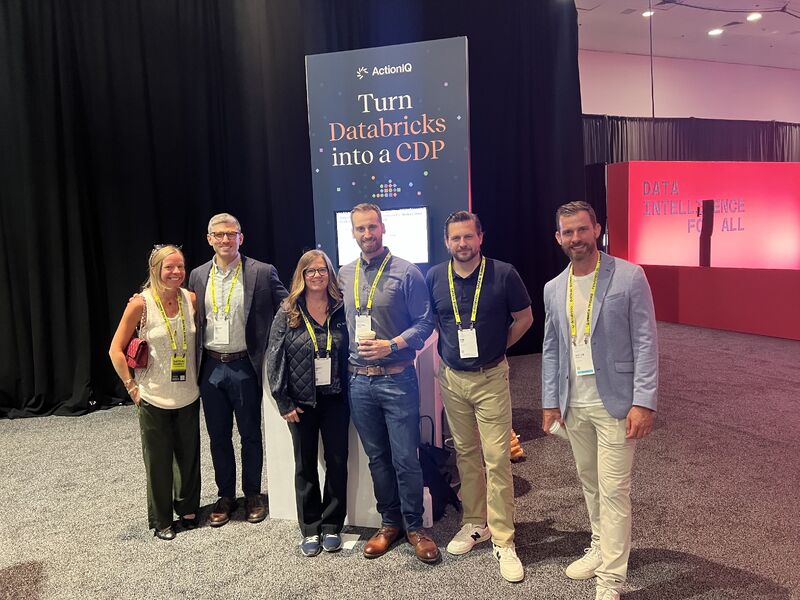 Leah Pope and ActionIQ colleagues at the 2024 Data and AI Summit beside a sign reading Turn Databricks into a CDP
