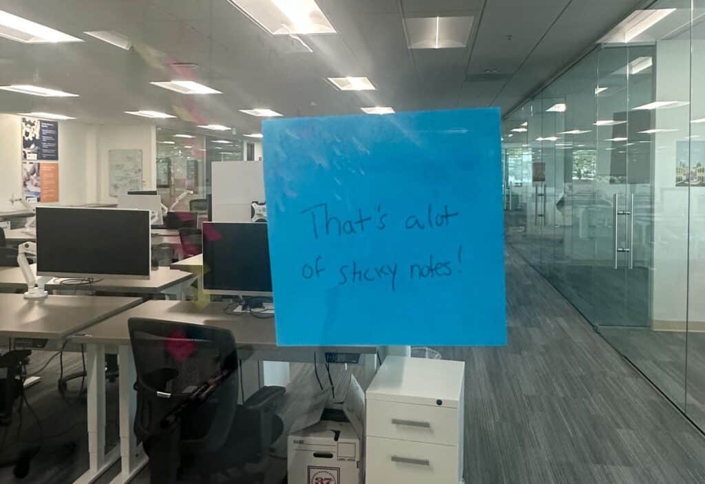 A large blue sticky note on a glass office wall, pictured in LeanTaaS’s 2024 company kickoff account