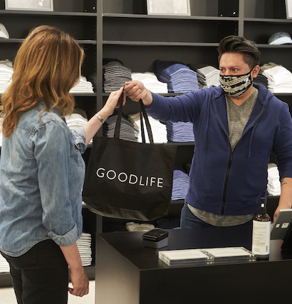 A Goodlife associate hands a shopping bag to a customer at the checkout