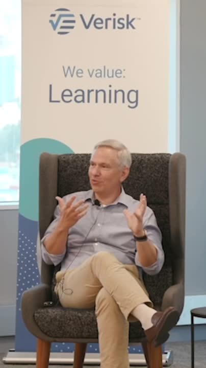 Lee Shavel seated in an armchair during a Verisk interview, with a Learning banner behind him