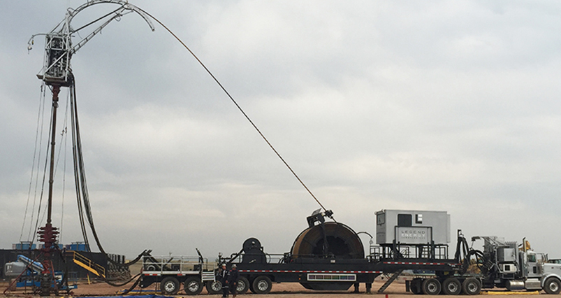 A Legend-branded coiled tubing unit with a large reel, injector structure and truck at an outdoor worksite