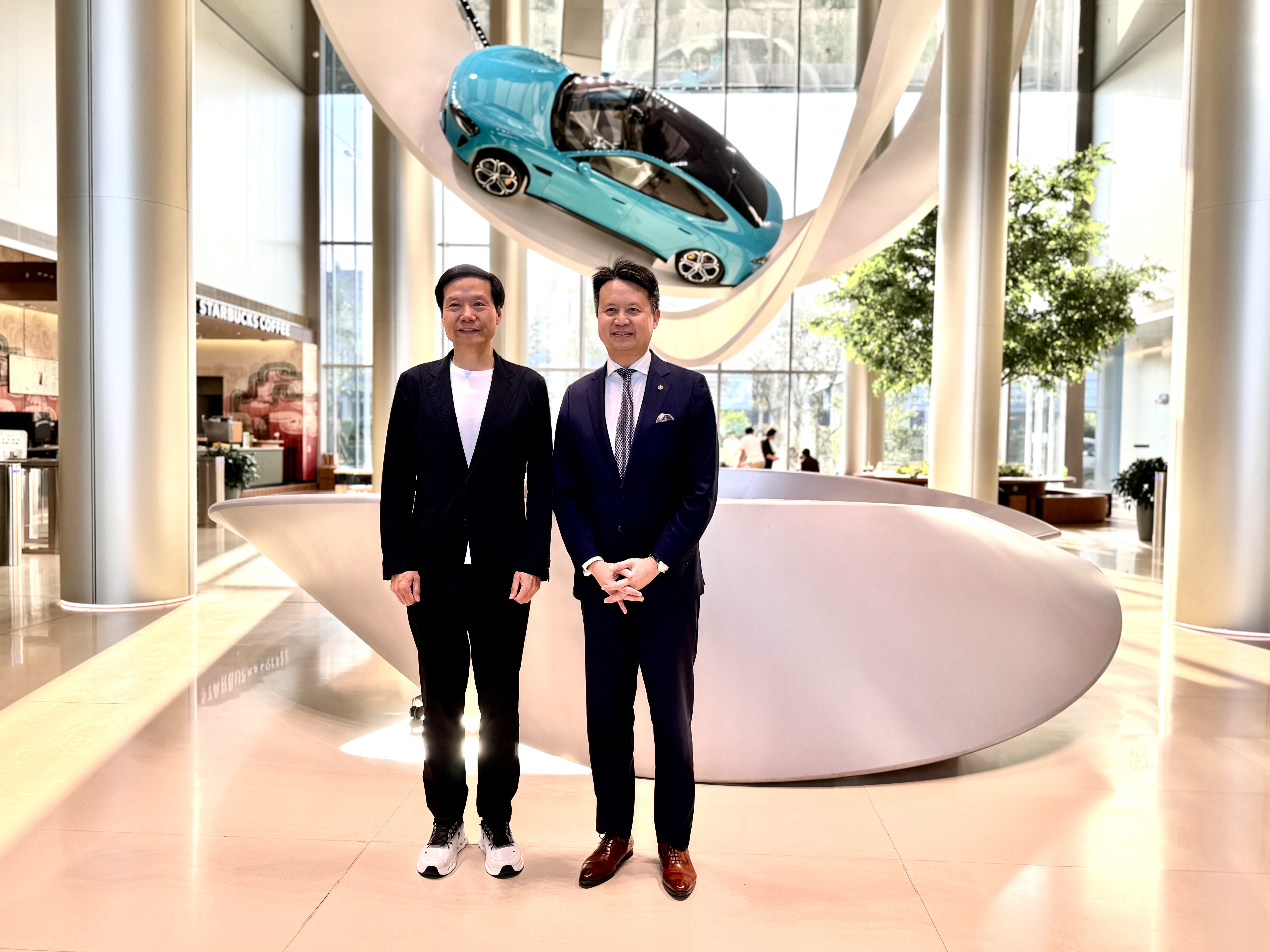 Lei Jun, left, with WIPO director general Daren Tang beneath a suspended blue Xiaomi car during a visit to the EV plant in Beijing.
