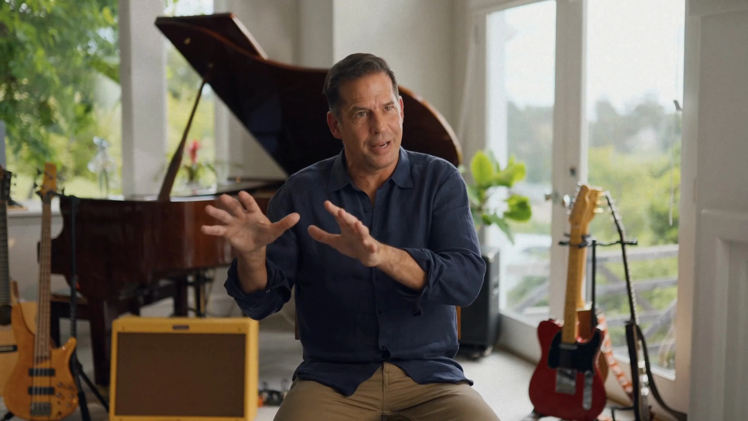 Leif Welch seated between guitars, an amplifier and a grand piano