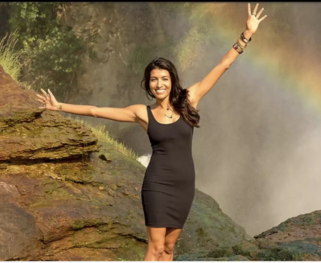 Leila Janah smiling with her arms outstretched beside a waterfall