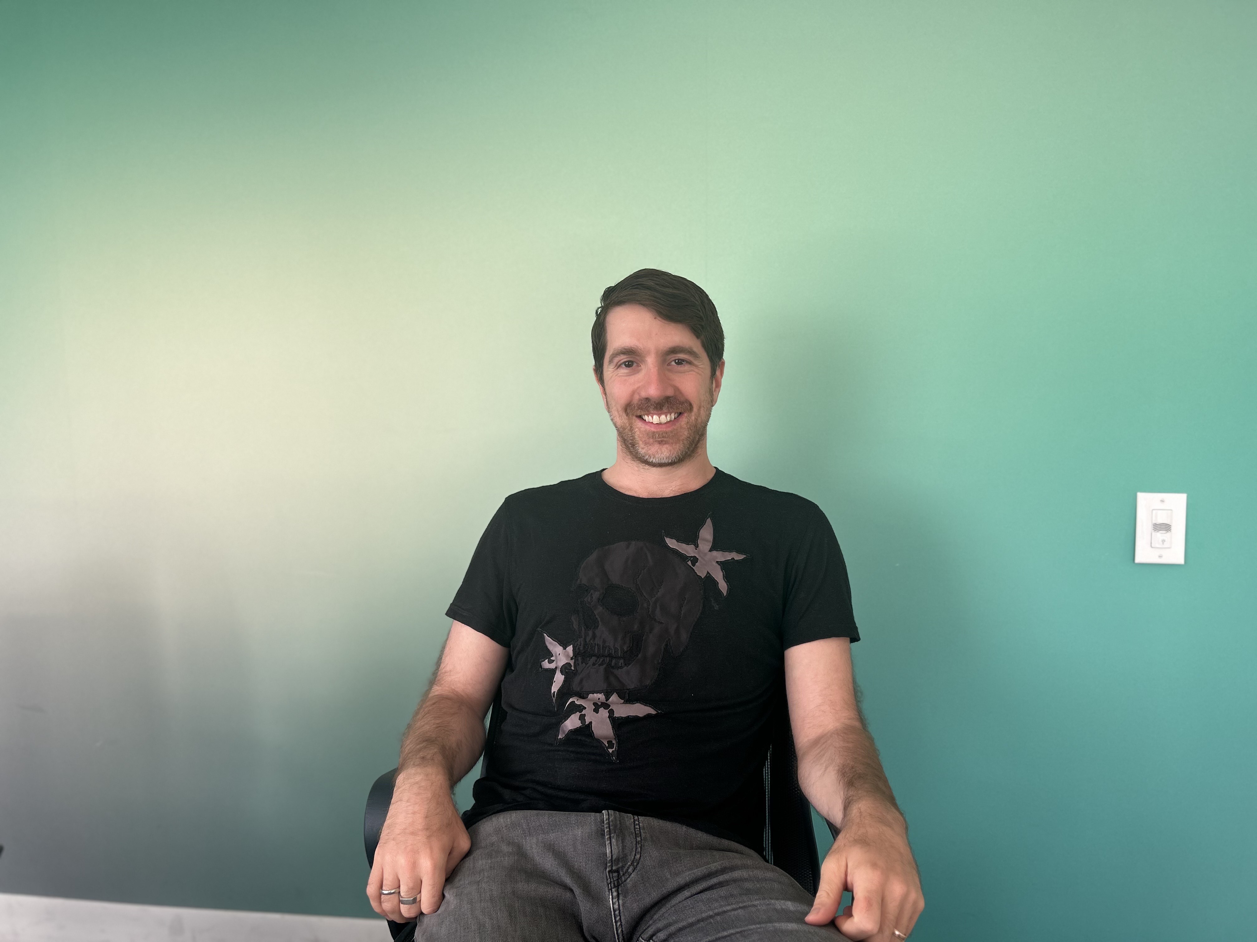 Leo Efstathiou seated in the FINSIGHT office against a green wall