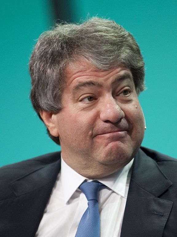 Leon Black wearing a suit and headset microphone against a green background
